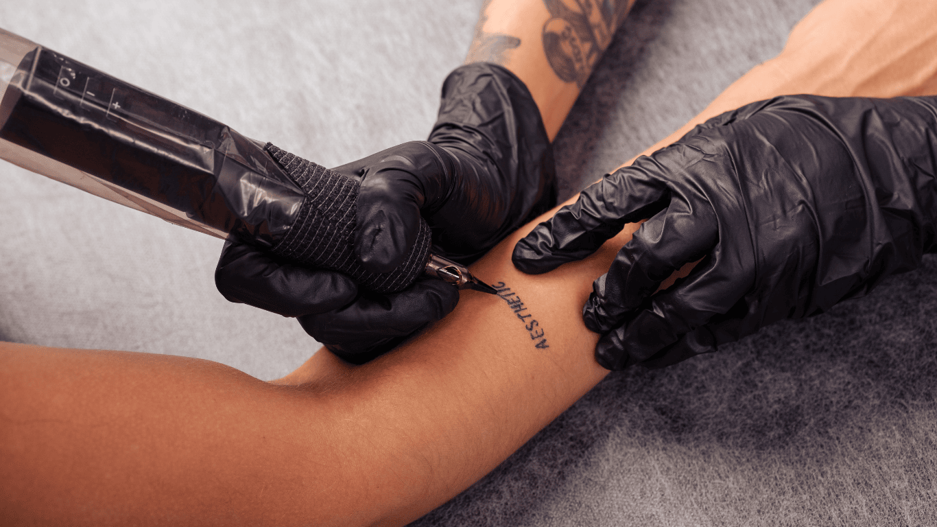 Tatuador tatuando la palabra aesthetic en el antebrazo a una chica